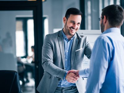 Two smiling businessmen shaking hands while standing in an office.